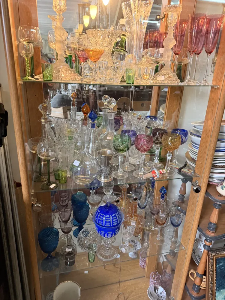 Collection de verres colorés et cristallerie ancienne dans une vitrine de brocante